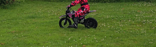 Child in a helmet riding a pink Kubbi electric dirt bike on grass