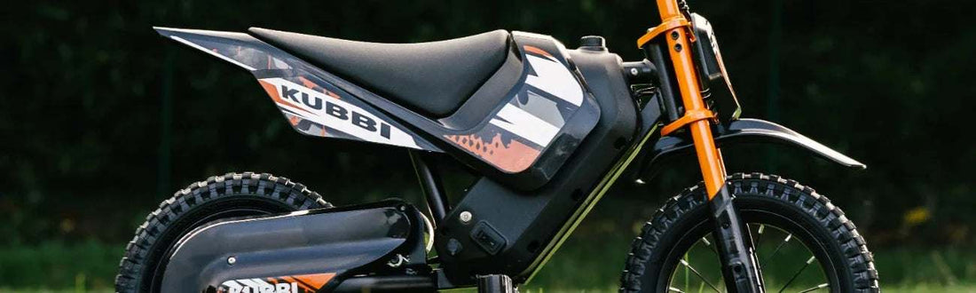 Side view of a Kubbi kids' electric dirt bike in orange and black, showing the frame, forks and seat