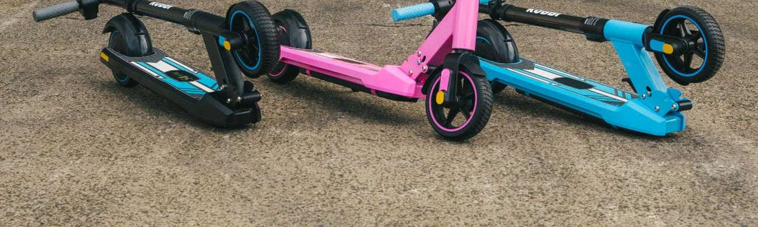 Three Kubbi kids’ electric scooters folded on tarmac in black, pink and blue