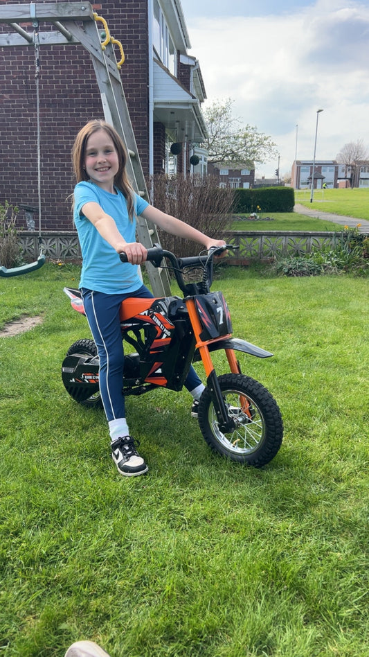 Kid riding a Kubbi electric dirt bike outdoors on a sunny day