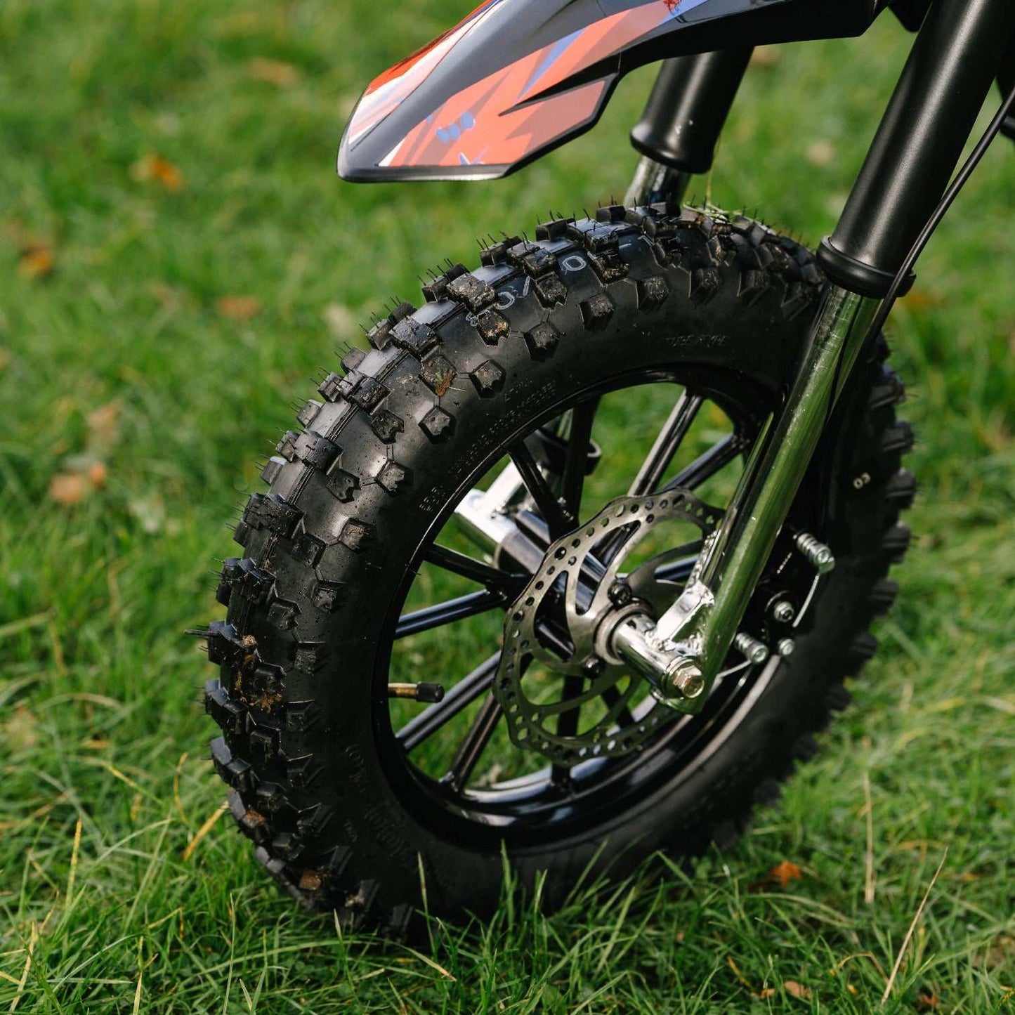 Close-up of Kubbi K10 Pro kids electric dirt bike's front 14-inch off-road tire and suspension on grass